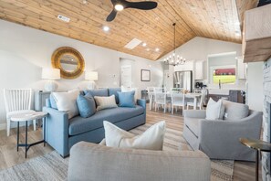 A modern living room with a blue sofa, grey armchairs, and a dining area with white chairs.