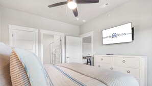 A bedroom with a bed, a dresser, a television mounted on the wall, and a ceiling fan. - New Home in Trophy Run with Private Hot Tub & Firepit, Near Taneycomo & Table Rock, Free Tickets (Branson)