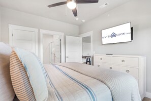 Ein Schlafzimmer mit einem Bett, einem Schminktisch, einem an der Wand montierten Fernseher und einem Deckenventilator.