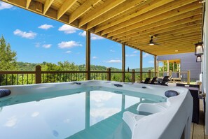 A hot tub under a wooden pergola with a view of a forested landscape.