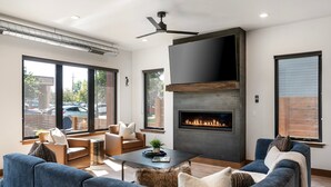 A modern living room with a fireplace, comfortable seating, and large windows. - New! Home Again Luxury Haven - Sleeps 8 (Whitefish)