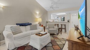 A living room with a sofa, ottoman, and striped armchair, a TV, and a ceiling fan. - Condo in Bonita! 2 Miles to the Beach! Beach Shuttle Included! (Bonita Springs)