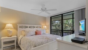 A bedroom with a bed, nightstands, a ceiling fan, a TV, and a balcony with a view of the beach. - Condo in Bonita! 2 Miles to the Beach! Beach Shuttle Included! (Bonita Springs)