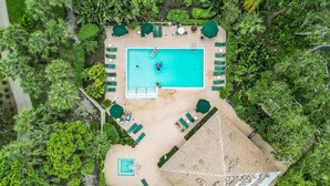 An aerial view of a resort with a swimming pool surrounded by lounge chairs and umbrellas, a separate pool area, and lush greenery. - Condo in Bonita! 2 Miles to the Beach! Beach Shuttle Included! (Bonita Springs)