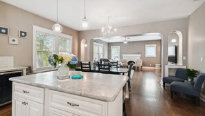 A spacious kitchen with a marble countertop, white cabinets, and a dining area with a table and chairs.