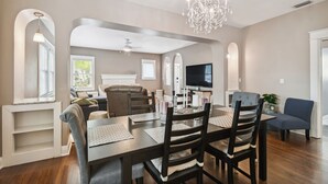 A modern living room with a dining area, featuring a chandelier, a flat-screen TV, and a comfortable seating arrangement.