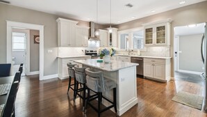 A spacious kitchen with white cabinetry, a central island with bar stools, pendant lighting, and a stainless steel refrigerator.