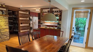 A spacious kitchen with a wooden dining table and chairs, a built-in oven, and a view of the garden through a glass door. - Spacious In-Town Retreat (Lewisburg)