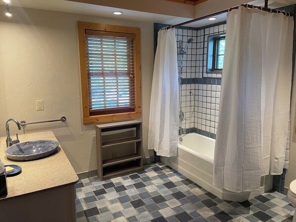 A bathroom with a bathtub, a shower, a sink with a marble basin, a window with blinds, and a checkered floor.