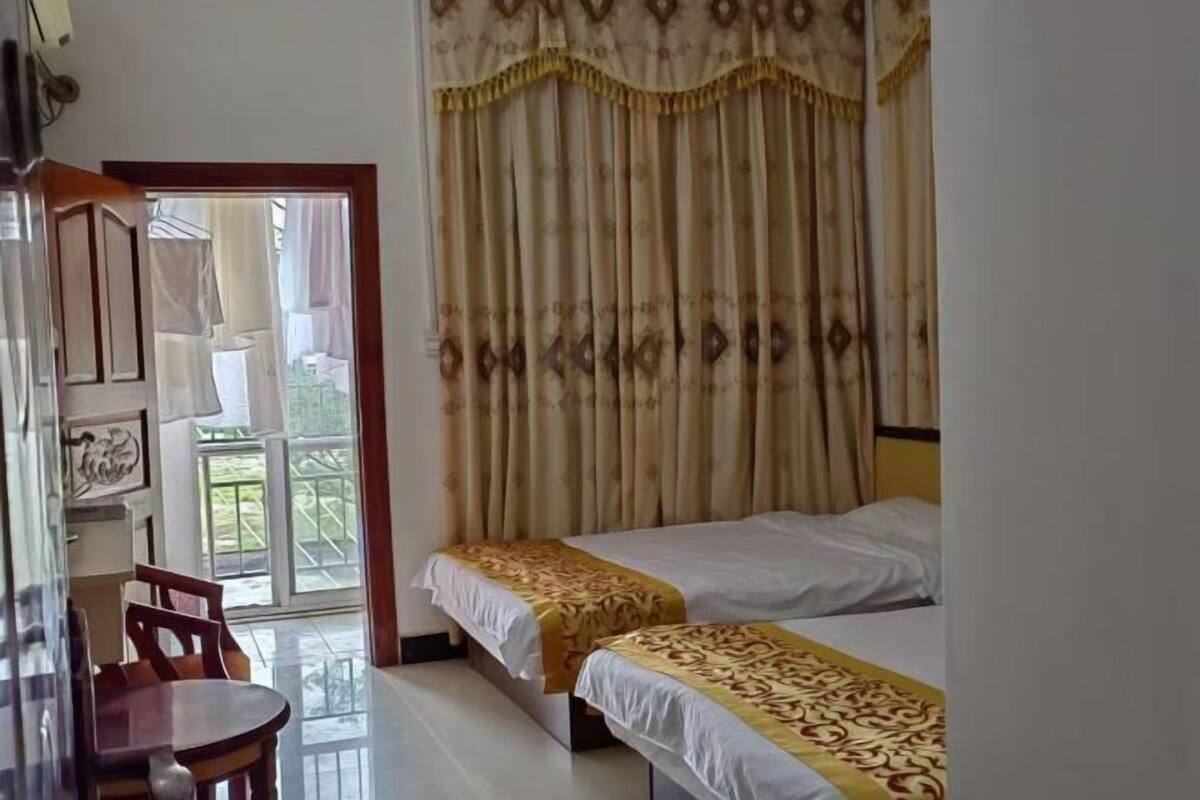 A room with two beds, a wooden chair, a table, and a view of a balcony.