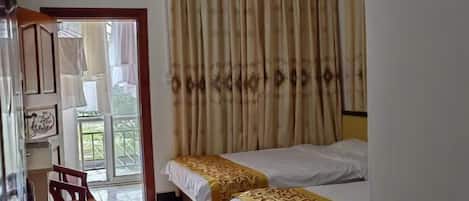 A room with two beds, a wooden chair, a table, and a view of a balcony.