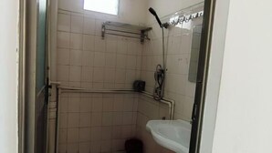 A small, tiled bathroom with a toilet, a red bucket, and a white sink. - Dongxing Wanwei Jintan Xiangyue Hotel (Dongxing)