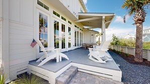 A covered outdoor seating area with Adirondack chairs, a small table, and a flag. - Shared Resort Style Pools, Boardwalk to the Beach, Golf Cart Access (Port Aransas)