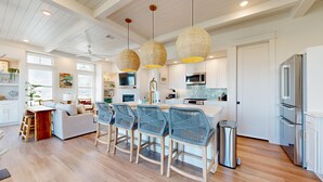 A modern kitchen with white cabinets, a stainless steel refrigerator, and a dining area with wicker chairs and a wooden table. - Shared Resort Style Pools, Boardwalk to the Beach, Golf Cart Access (Port Aransas)