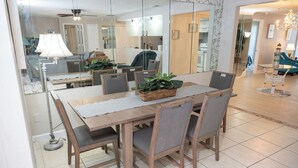 Een eethoek met een houten tafel, grijs gestoffeerde stoelen en een gevlochten mand met planten.