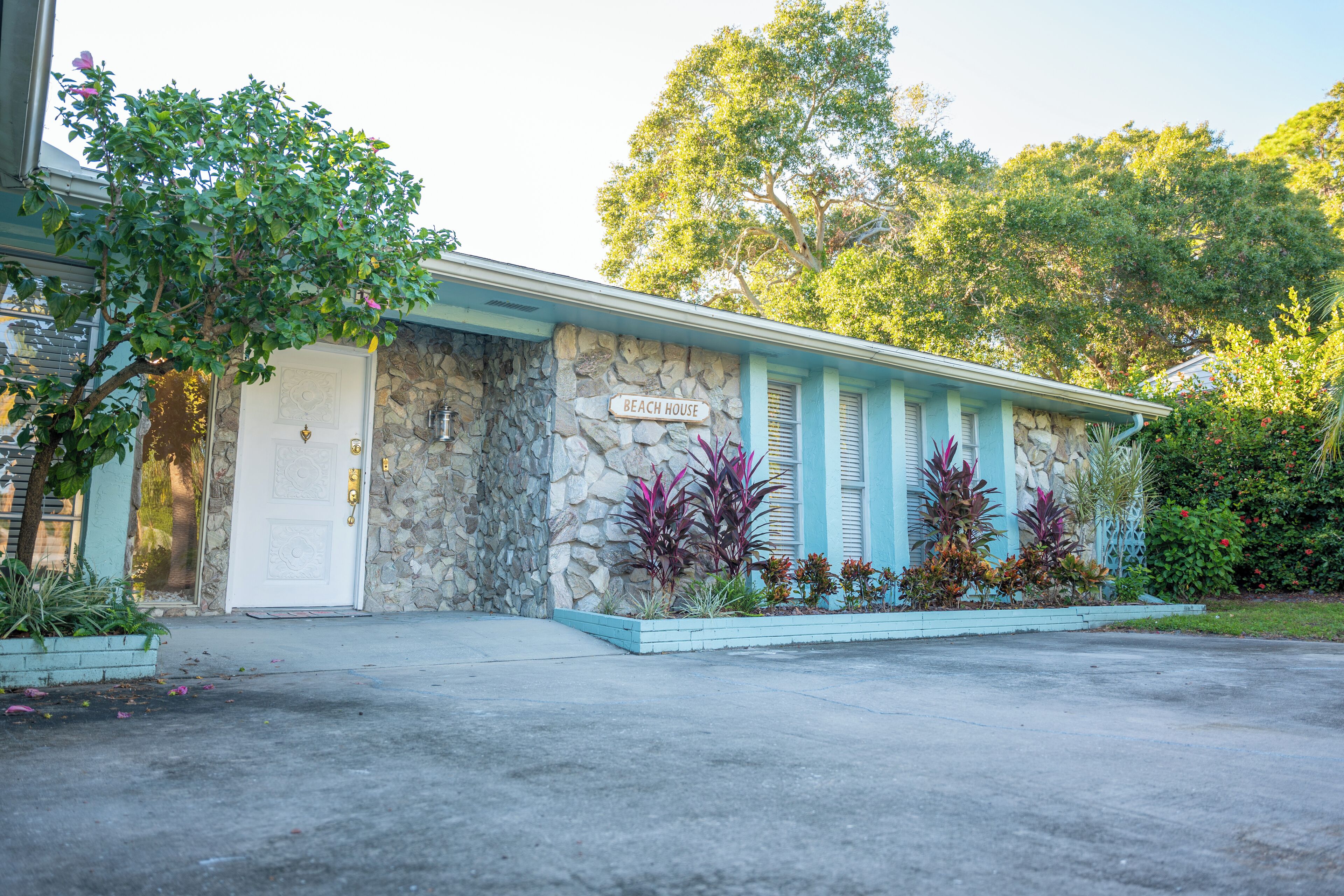 Una casa de playa con fachada de piedra, una puerta blanca y un cartel que dice 'BEACH HOUSE'.