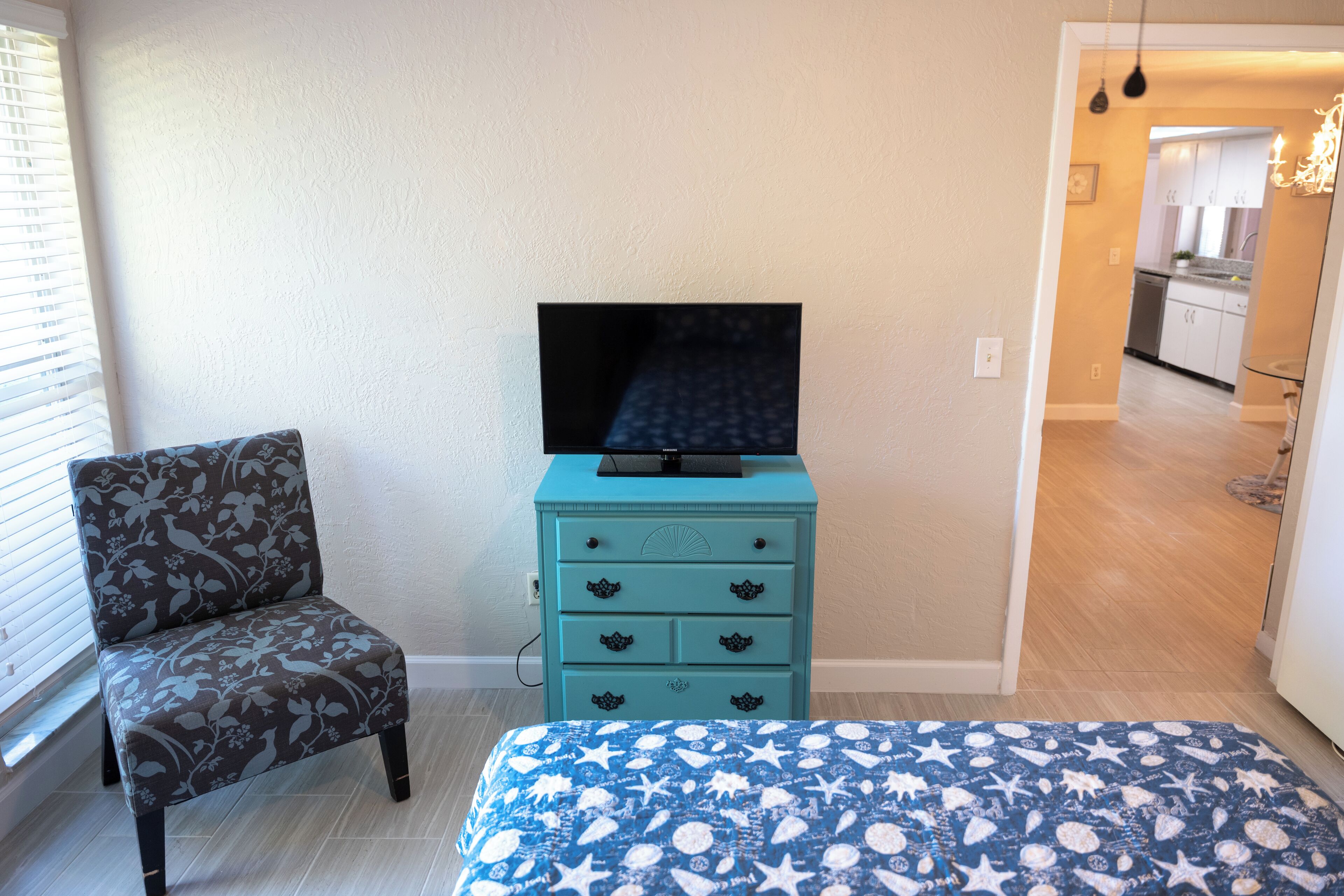 A bedroom with a bed, a chair, a dresser, and a TV.