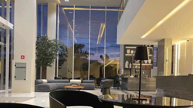 A modern lobby with a glass wall, a reception desk, and a seating area with sofas and a coffee table. - Riva Apart Hotel (Campo Mourao)