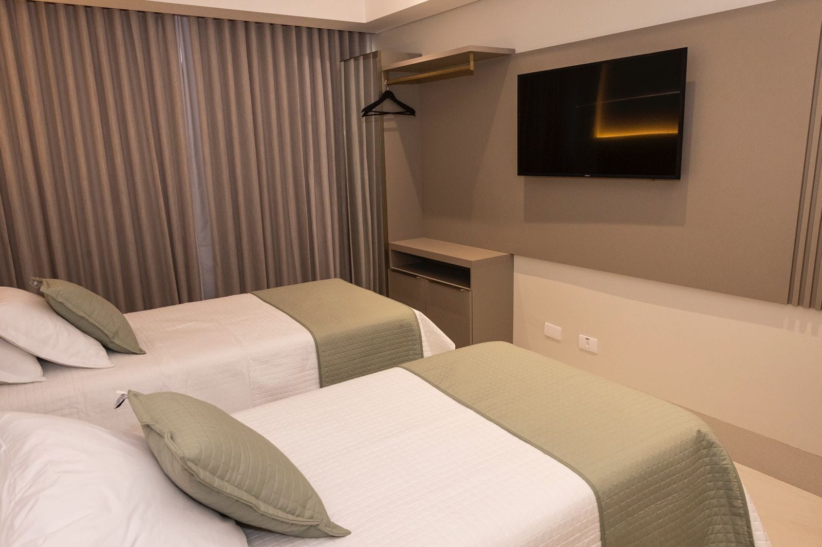 A hotel room with two beds, a TV, a coat rack, and a small desk.