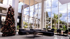 A modern hotel lobby with a large Christmas tree, a black leather sofa, and a glass coffee table. - Riva Apart Hotel (Campo Mourao)
