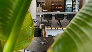 A modern bar area with a wooden wall, a refrigerator stocked with beverages, and several black chairs. - Riva Apart Hotel (Campo Mourao)