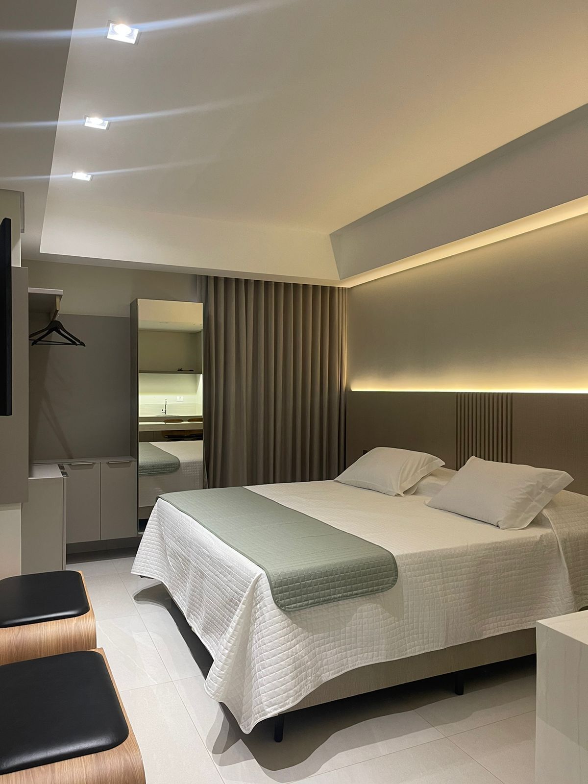 A modern hotel room with a large bed, bedside tables, a mirror, and a wardrobe.