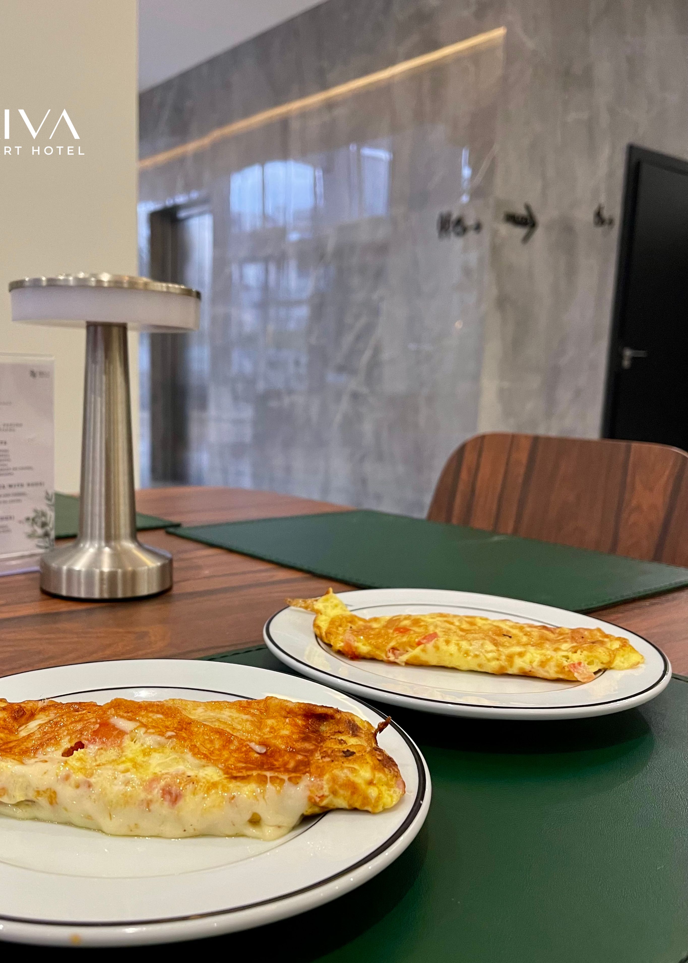 A dining table with two plates of omelette, a menu, and a candle.