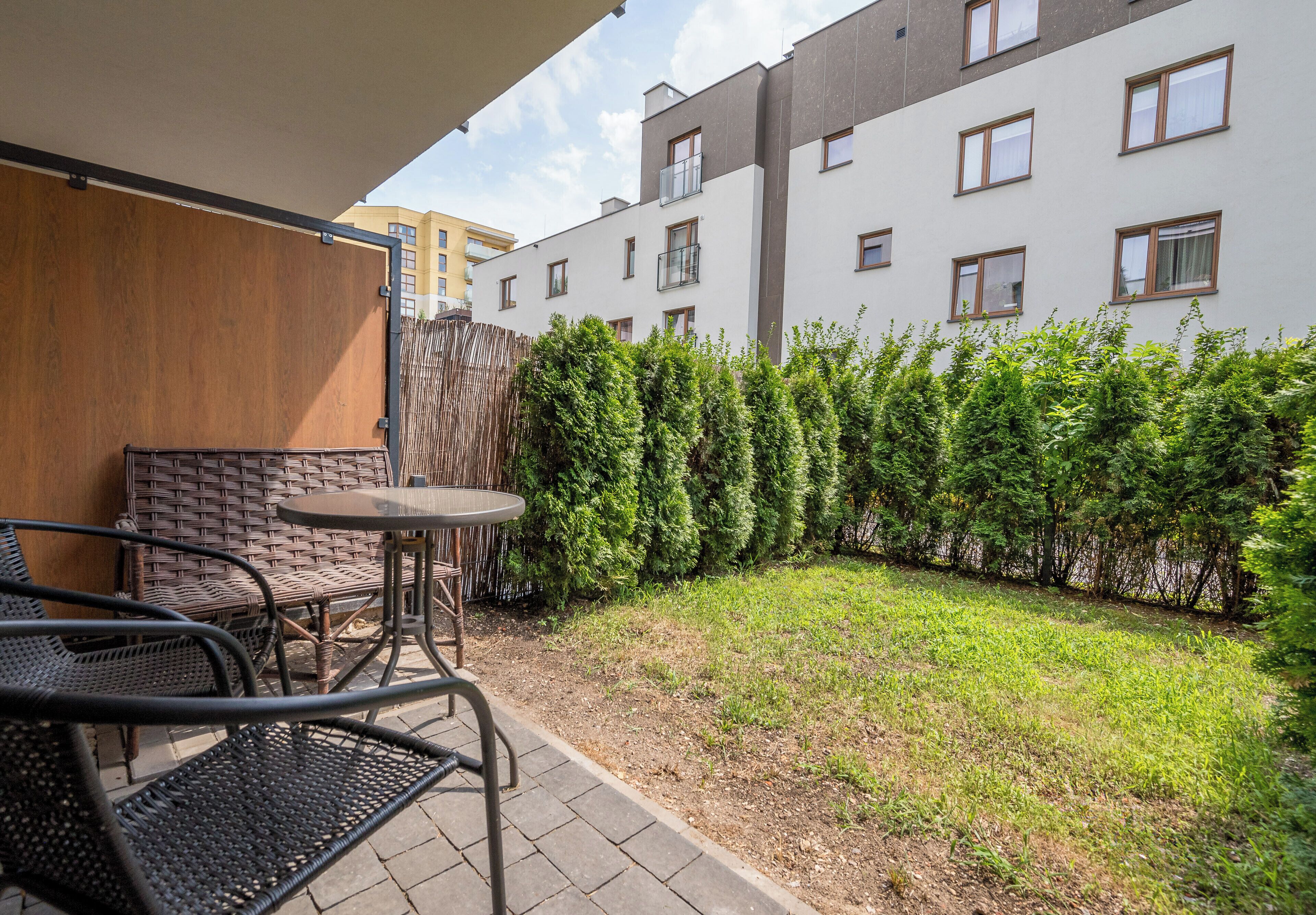 A courtyard with a seating area, a wooden wall, and a hedge.