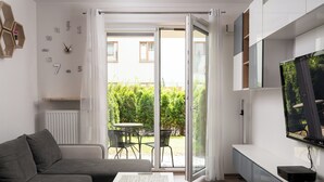 Ein modernes Wohnzimmer mit grauem Sofa, Couchtisch, Flachbildfernseher und einer Schiebetür zu einer Terrasse mit Tisch und Stühlen.