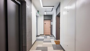 Ein moderner Flur mit einem Schachbrettfußboden, einer Holztür am Ende und einer Leuchte an der Decke.