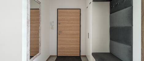 Un pasillo con una puerta de madera, un espejo y un banco gris.
