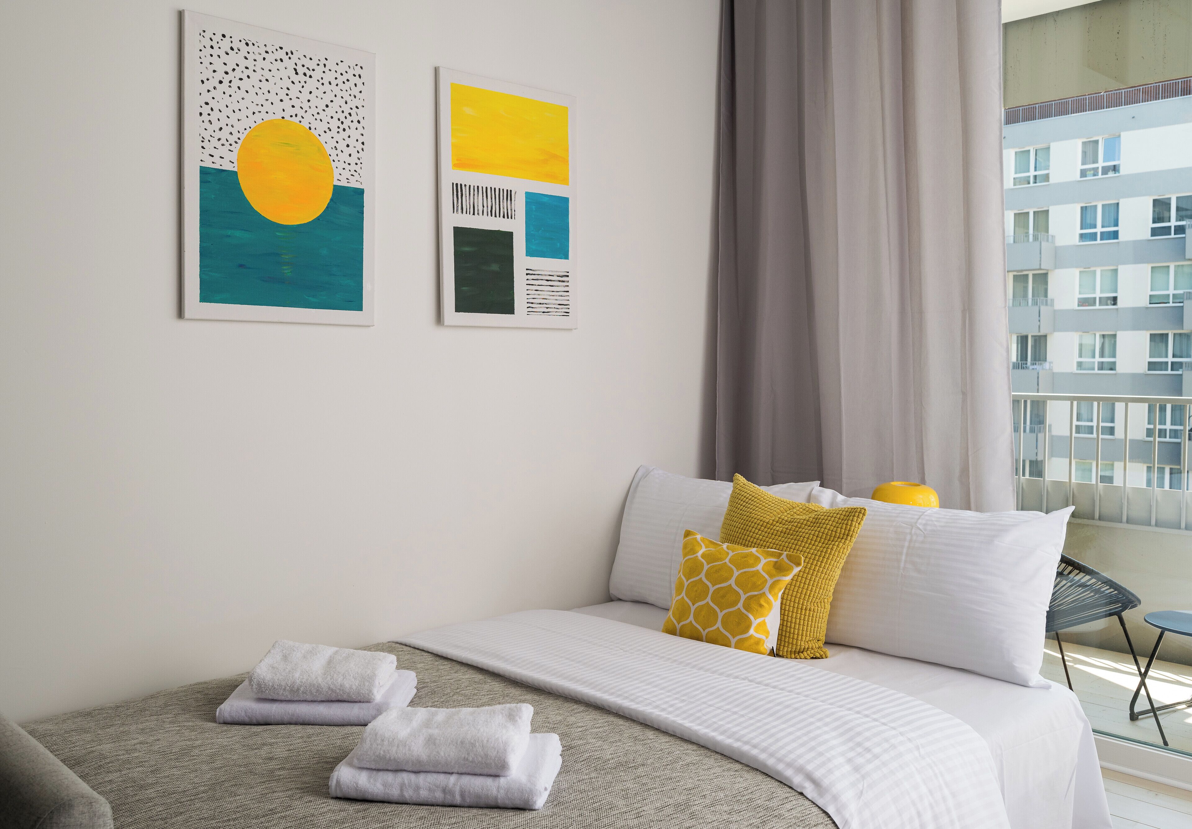 Habitación de hotel moderna con una cama, dos obras de arte en la pared y vista a la ciudad por la ventana.