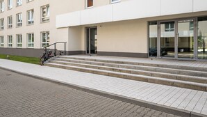 Ein Gebäude mit moderner Fassade, einer Treppe aus Beton, die zu einem Glastür-Eingang führt, und einem Fahrrad, das am Gehweg steht.