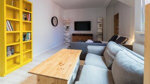 A modern living room with a sofa, a wooden coffee table, a yellow bookshelf, a wall-mounted TV, and a hanging light fixture. - Głogowska Spacious Apartment (Poznań)