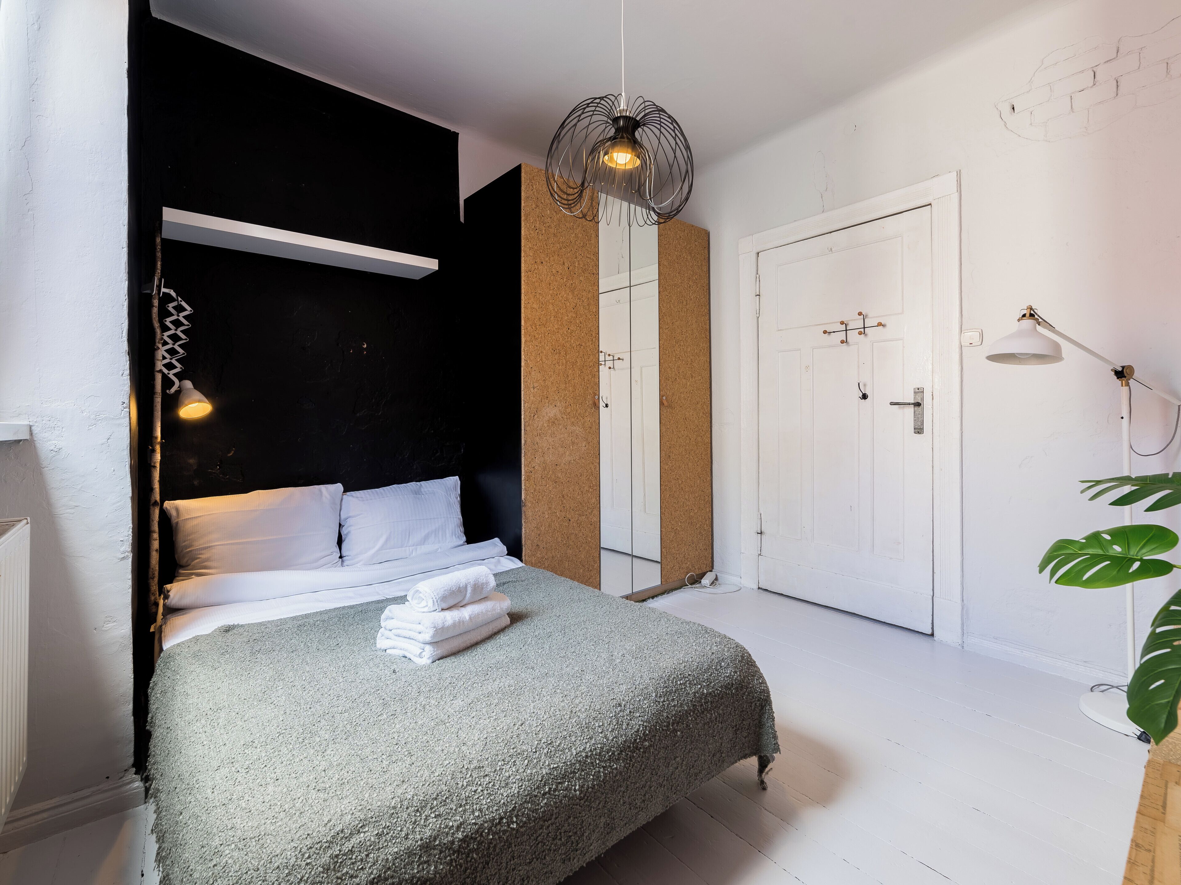 A bedroom with a bed, a hanging light fixture, a door, and a plant.
