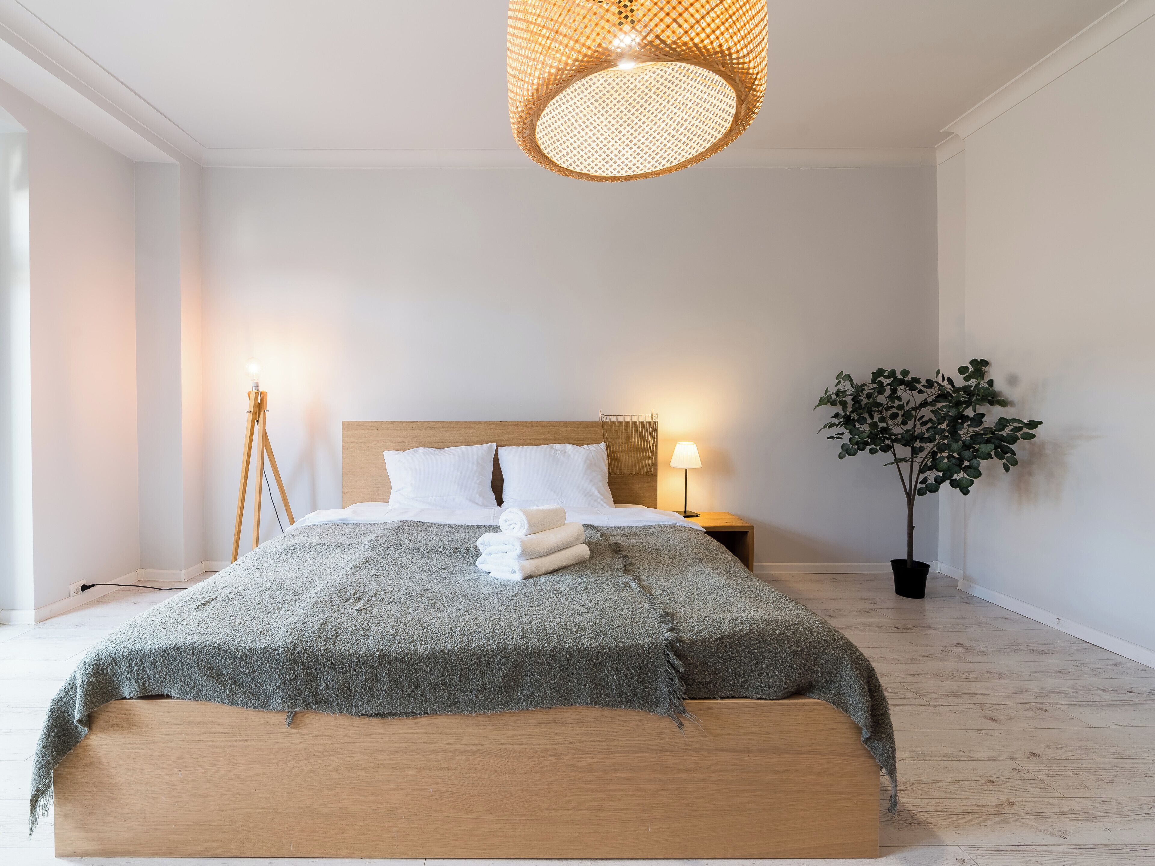 Un dormitorio moderno con una cama de madera, una lámpara colgante tejida de gran tamaño, una mesita de noche con lámpara y una planta en maceta.