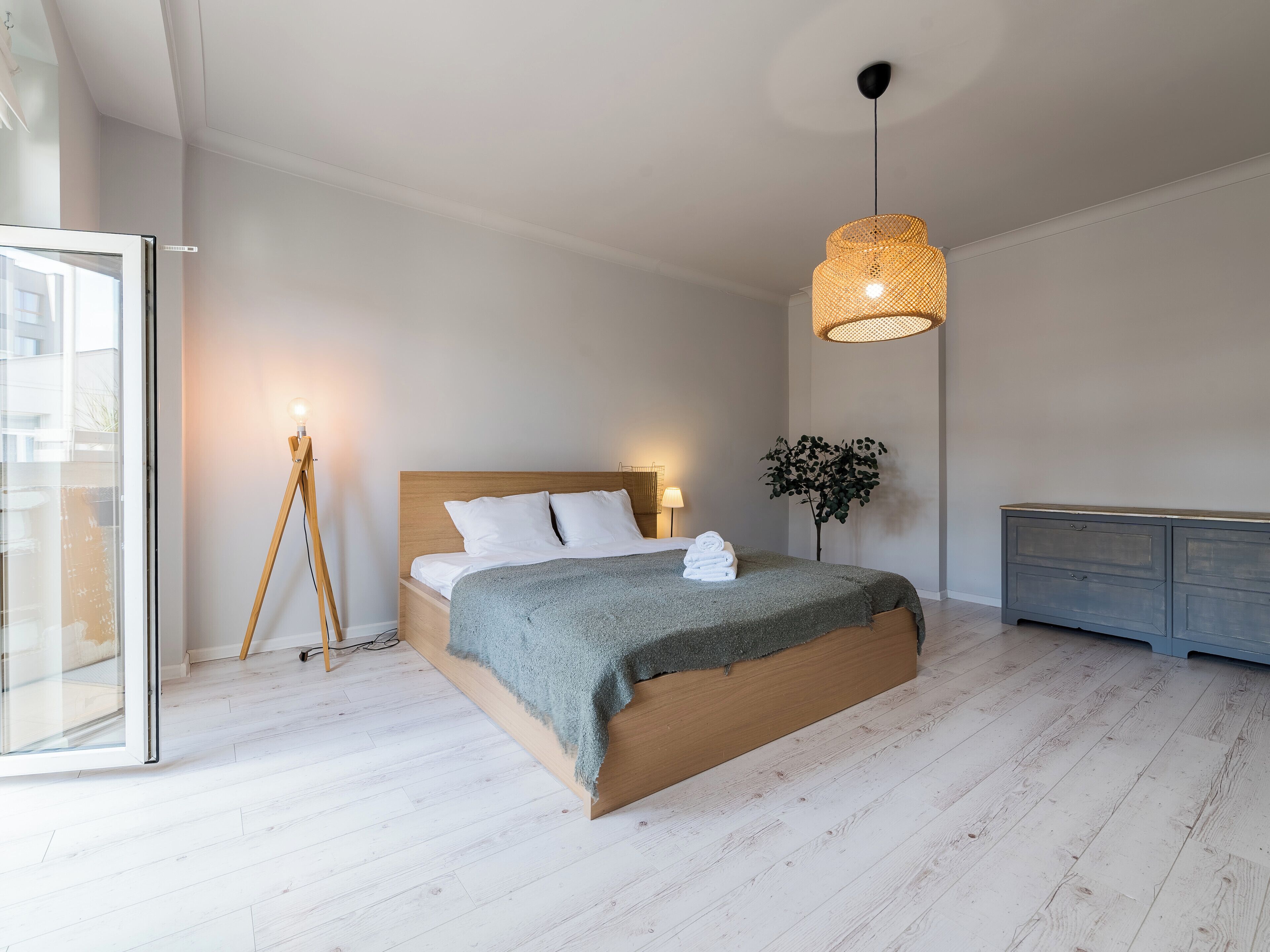 A modern bedroom with a wooden bed, a floor lamp, a hanging light fixture, and a grey cabinet.