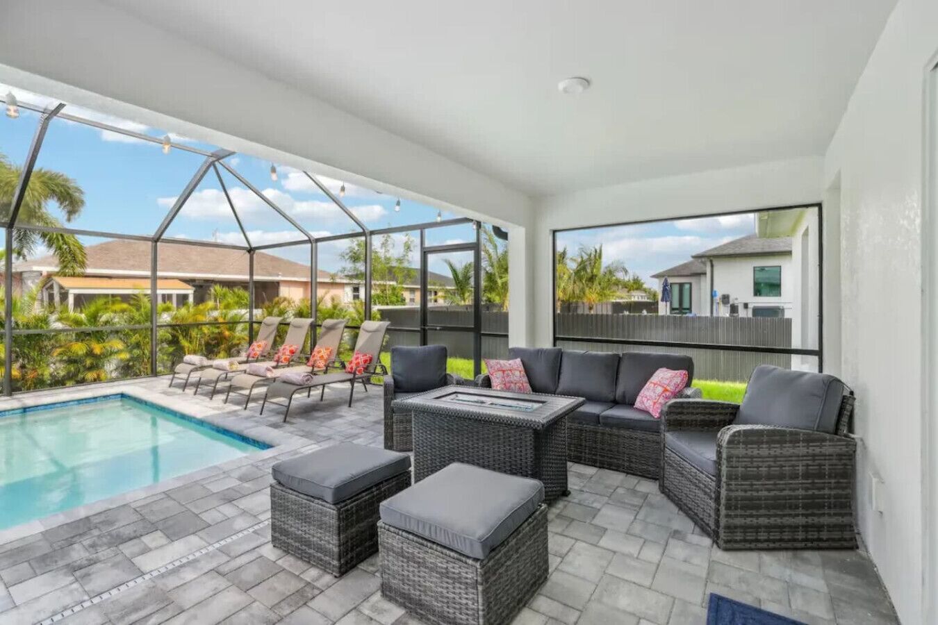 A covered outdoor area with a pool, lounge chairs, and a sofa with cushions.