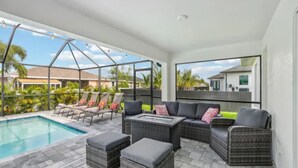Ein überdachter Außenbereich mit Pool, Liegestühlen und einer Couch mit Kissen.