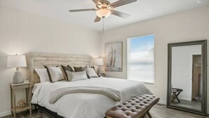 Ein Schlafzimmer mit einem großen Bett, einem Deckenventilator, einer Bank und Meerblick durch ein Fenster.