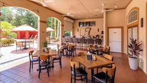 A covered outdoor dining area with multiple tables and chairs, a bar area, and a view of the surrounding greenery. - Remodeled 3 bed / 2 bath near Disney (Davenport)