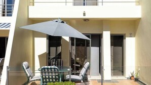 A modern building with a glass door entrance, a balcony with a table and chairs, and a large umbrella. - Villa Emilly (Albufeira)