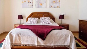 A neatly made bed with a wooden headboard, two matching pillows, and a red throw blanket. There are two bedside tables with lamps and a wall-mounted power outlet. - Villa Emilly (Albufeira)