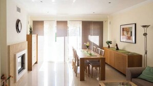 A spacious living room with a dining area, a fireplace, and a modern kitchen visible through a glass door. - Villa Emilly (Albufeira)