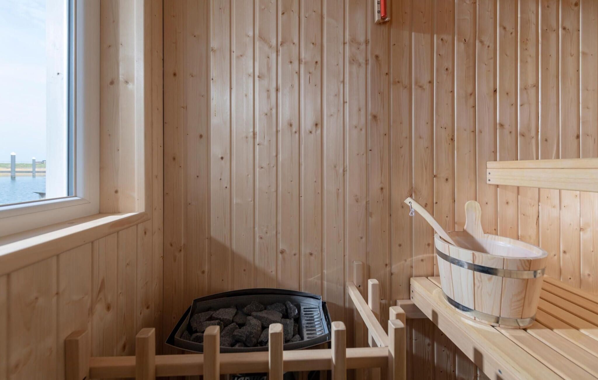 Una sala de sauna con paredes de madera, una ventana, un banco de sauna y un cubo.