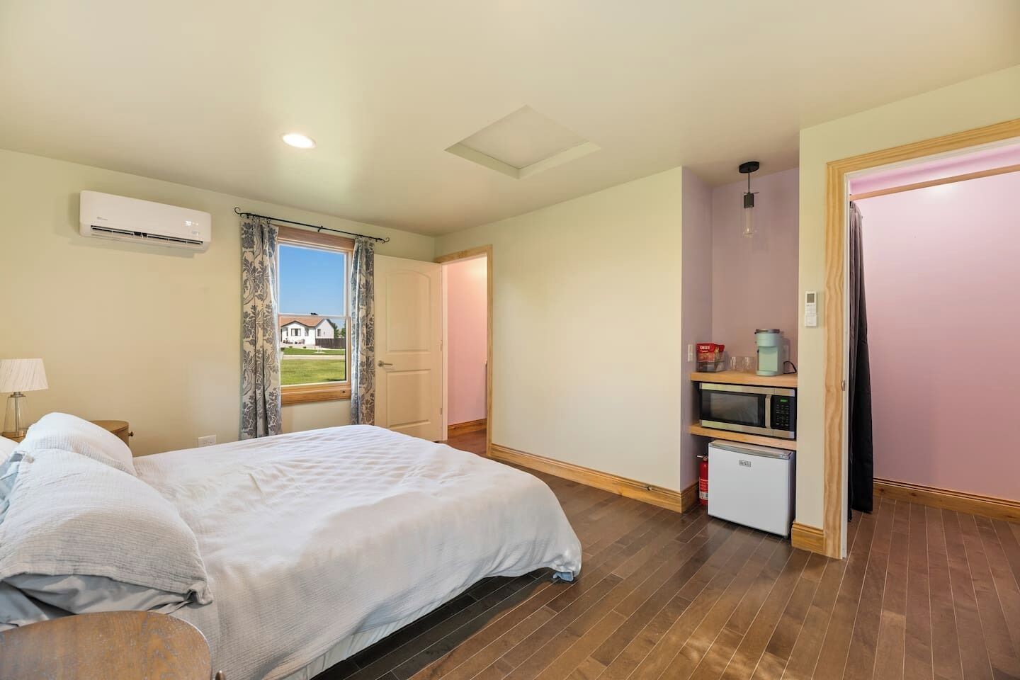 Quarto de hotel com cama, escrivaninha, micro-ondas e pequena geladeira.