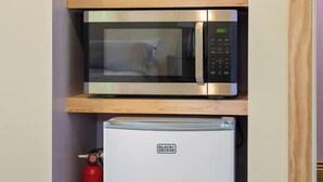 Una kitchenette compacta con microondas, un refrigerador pequeño, una cafetera y un extintor.