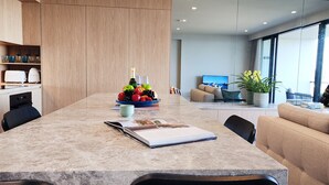 Un comedor moderno con una mesa de mármol, un centro de mesa con frutas y un sofá al fondo.