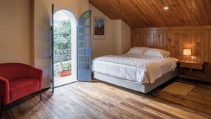 A bedroom with a wooden ceiling, a bed with white bedding, a red chair, and a door leading to a balcony with potted plants. - Suite de Lujo en Casa Patrimonial Reformada, en Zona Céntrica (Cuenca)