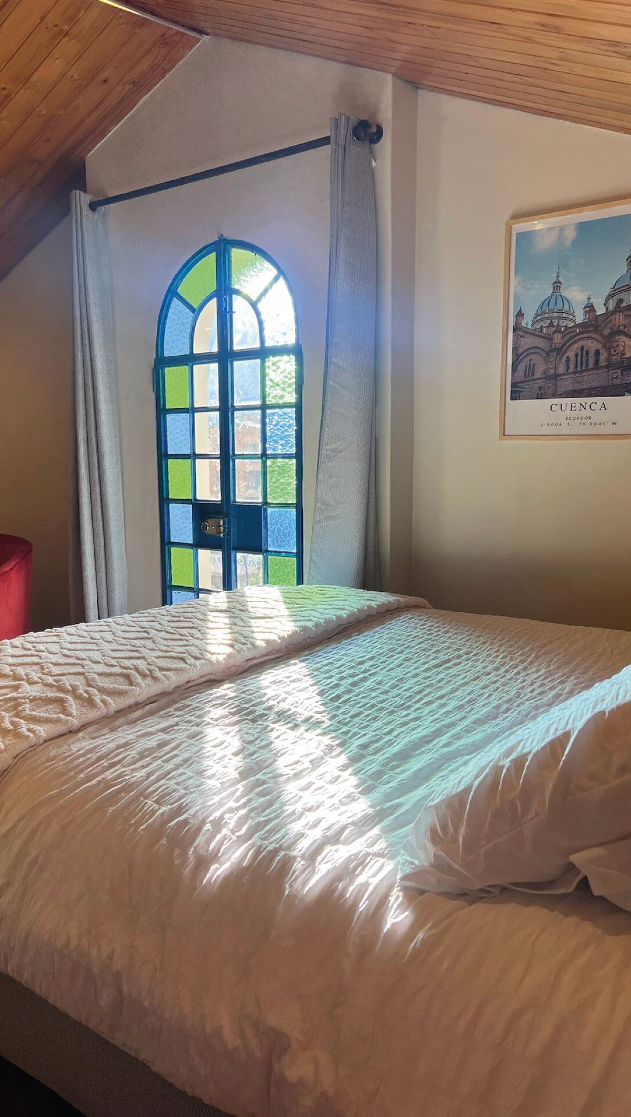 A bedroom with a bed, a window with curtains, and a framed picture of a building.